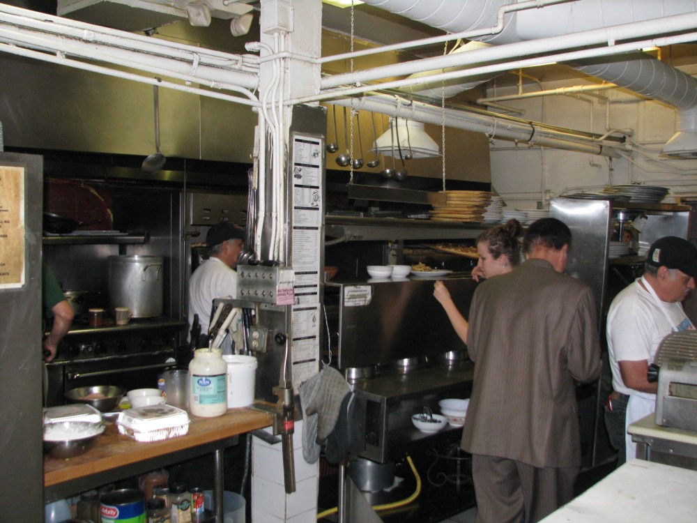 A cozinha. Na porta dos fundos, também fica o estoque de merchan do bar